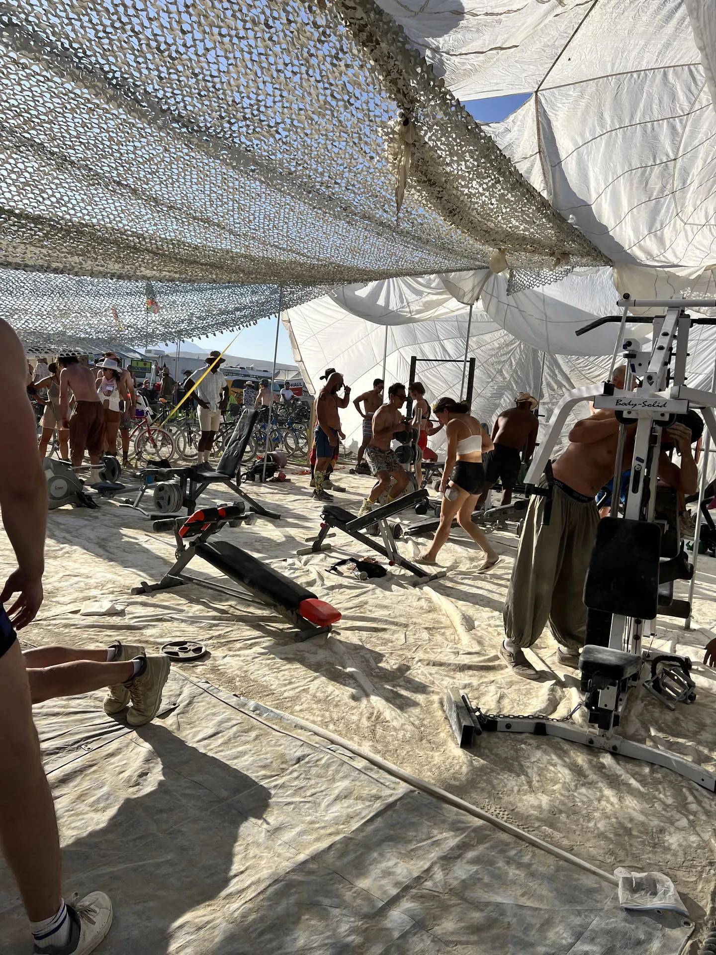 A makeshift gym with weight equipment under a large white shade structure.
