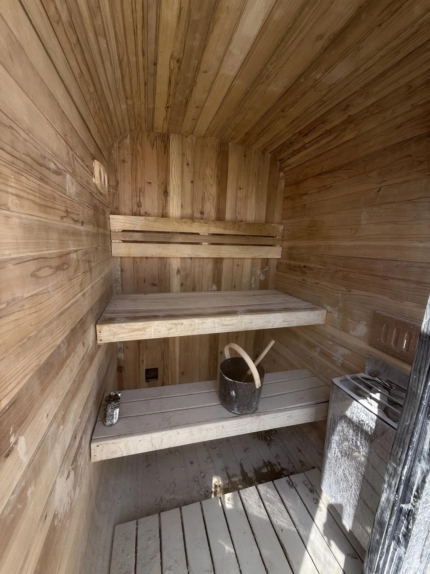 A wooden sauna interior with benches, bucket, ladle, and heater.